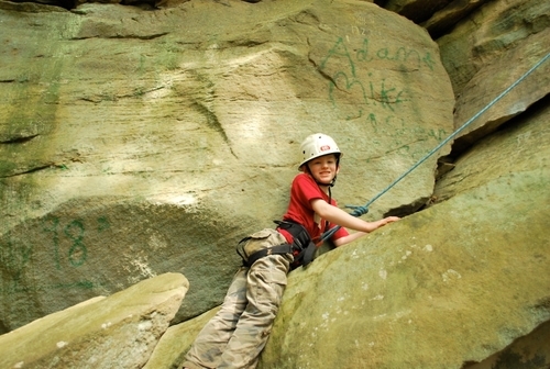 Camp climbing up large rocks with helment, harnest and rope.